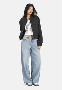 Czarna krótka kurtka z dwiema przednimi kieszeniami, zestawiona z biało-granatowym, w paski krótkim topem oraz jasnoniebieskimi spodniami typu wide-leg. Szare buty.