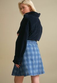 Marinblå kordjacka med hög krage, kombinerad med en ljusblå rutigt denimkjol med utsvängd nederkant och tonala knappar.