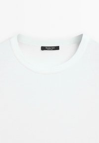 T-shirt blanc à col rond avec une étiquette noire à l’intérieur du col indiquant "Massimo Dutti Made in India."