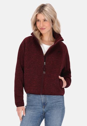 Burgundin värinen fleece-takki, jossa on korkea kaulus, täysipitkä vetoketju, kaksi sivutaskua ja teksturoitu neulekuvio. Yhdistetty valkoisen paidan ja sinisten farkkujen kanssa.