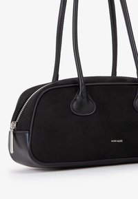 Borsa nera in suede e pelle, con forma arrotondata, doppie maniglie, zip argentata e un piccolo logo sulla parte anteriore.