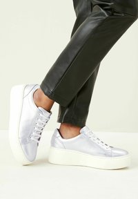 Silver leather sneakers with a textured finish, round toe, and white platform sole, paired with fitted black trousers.