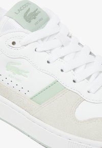 Zapatillas Lacoste de cuero y ante blanco, con acentos en verde menta, punta redonda, cordones planos y logotipo en relieve en la lengüeta.