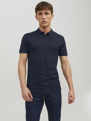 Polo shirt bleu marine en coton, avec un col classique, des manches courtes et un logo discret sur la poitrine, associé à un jean foncé.