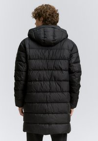 Abrigo largo acolchado negro con capucha, que presenta costuras horizontales y un corte relajado. La tela parece suave y resistente al agua.