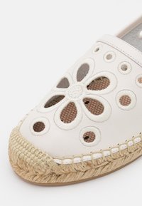 Chaussure espadrille blanche avec motifs floraux et circulaires découpés, dotée d'une semelle en jute tressée et de détails de couture visibles.