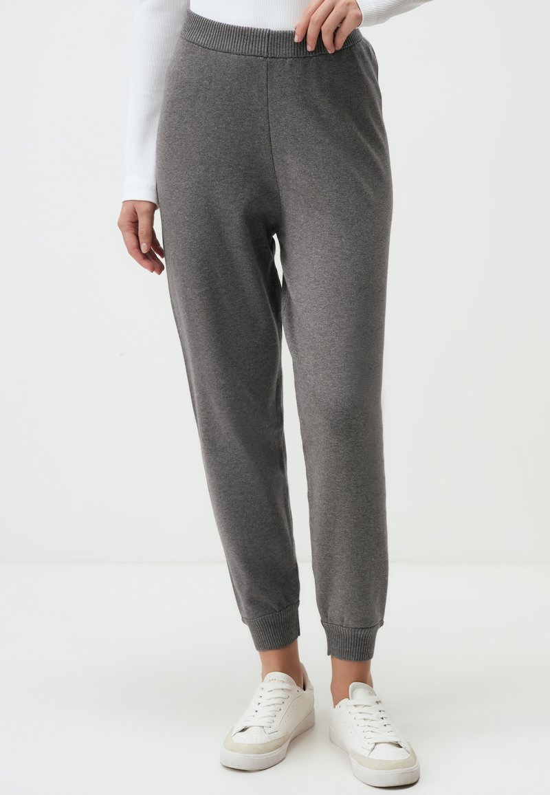 Graue Jogginghosen mit geripptem Bund und Bündchen, aus weichem Material gefertigt, kombiniert mit weißen Sneakers für einen lässigen Look.