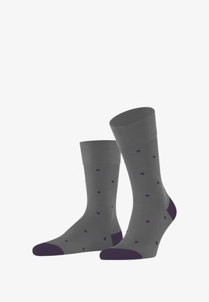 Graue Socken mit einem gerippten Bündchen und lila Punkten, mit einer dunkel-lila Spitze und Ferse, aufrecht gegen einen weißen Hintergrund präsentiert.