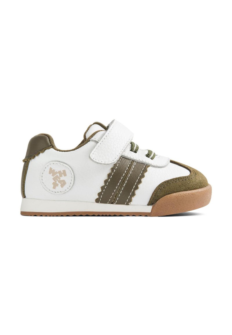 Fehér sportcipő zöld részletekkel, velúr orránál és sarkánál, fűzőkkel és tépőzárral, valamint mintás oldalakkal, melyeken kör alakú logó található.