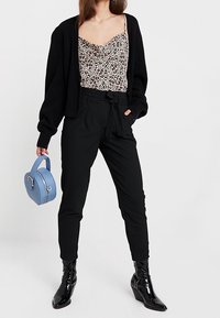 Cardigan nero oversize, canotta con stampa animale, pantaloni neri sartoriali, borsa tonda blu e stivaletti neri lucidi.