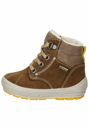 Botte de cheville en daim marron avec doublure en peluche blanche, semelle extérieure en caoutchouc jaune, lacets beiges et œillets en métal, avec une étiquette étanche.