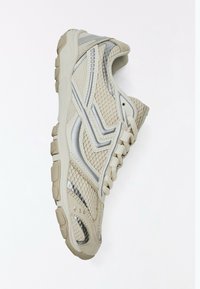 Basket de sport beige et argentée avec tissu en mesh, semelle coussinée et design à lacets, vue de profil.