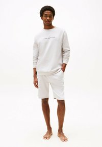 Felpa in cotone grigio chiaro con maniche lunghe e colletto rotondo, con logo "Tommy Hilfiger". Abbinata a pantaloni corti grigio chiaro coordinati.