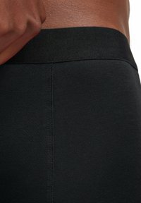 Leggings noirs ajustés en tissu lisse et extensible, avec une taille texturée et des coutures plates pour le confort et un volume minimal.