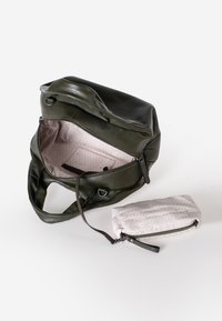 Donkergroene leren rugzak met een ritsluiting, voorzien van een geprinte roze binnenkant en een klein wit ritszakje. De textuur is glad.