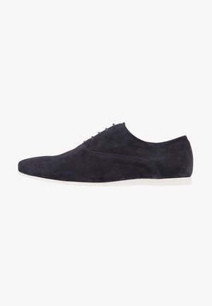Chaussures en daim bleu marine avec une texture lisse, un bout pointu et un design minimaliste. Comprend six œillets pour les lacets et une semelle blanche.