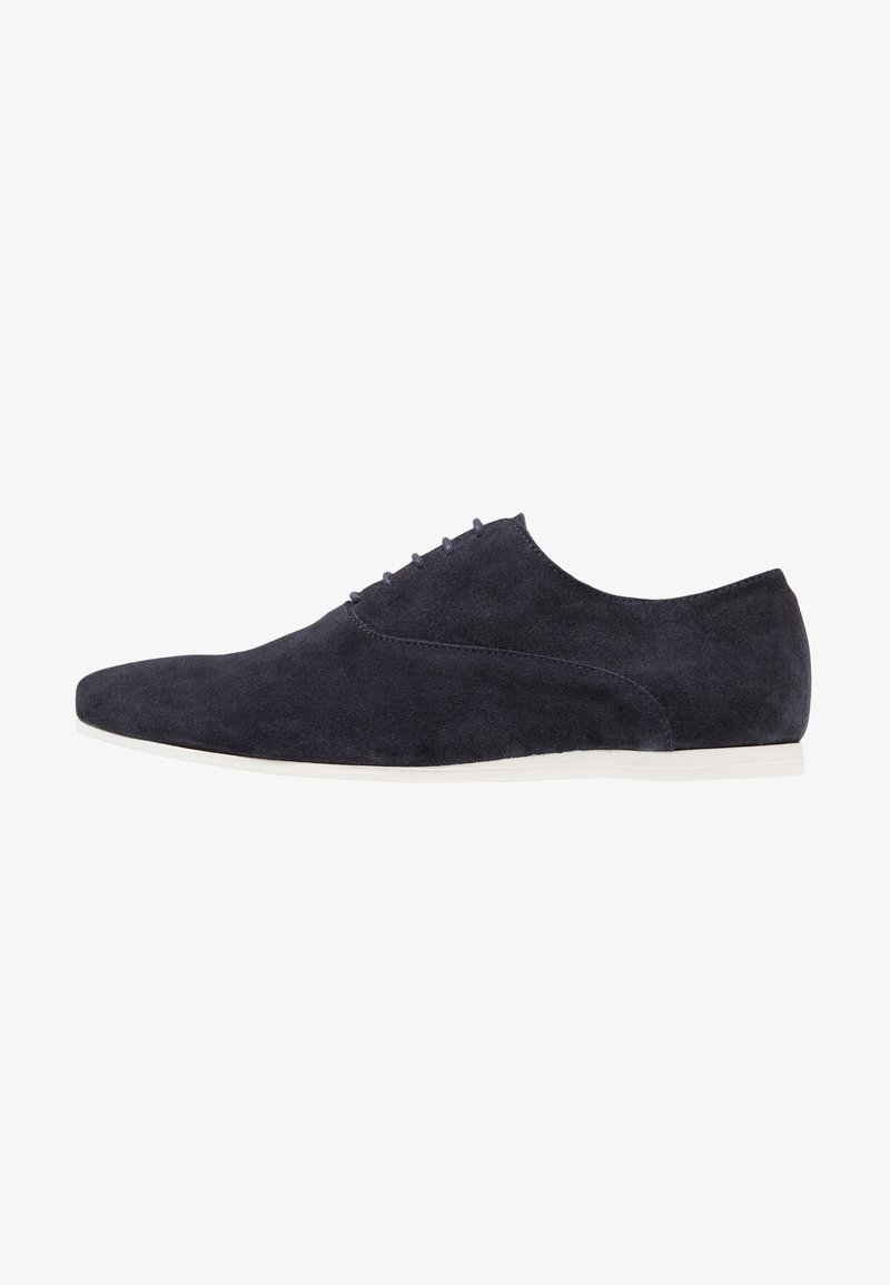 Chaussures en daim bleu marine avec une texture lisse, un bout pointu et un design minimaliste. Comprend six œillets pour les lacets et une semelle blanche.