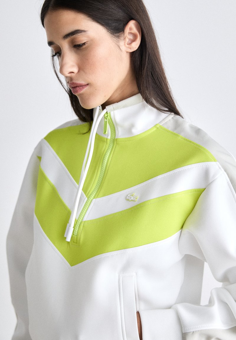 Weißer Quarter-Zip-Sweatshirt mit einem auffälligen Neon-Grünen Chevron-Design und einem kleinen gestickten Logo. Glattes Material mit Reißverschluss-Kragen.