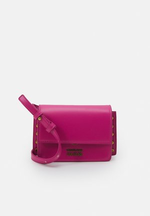 Kleine rechthoekige felroze leren crossbodytas met gouden studs langs de zijkanten en het "Versace Jeans Couture"-logo op de voorkant.