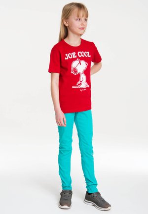 Rotes T-Shirt mit einem weißen Grafikdruck eines Cartoon-Charakters und dem Text "JOE COOL". Kombiniert mit türkisfarbenen Slim-Fit-Hosen und grauen Sneakers.