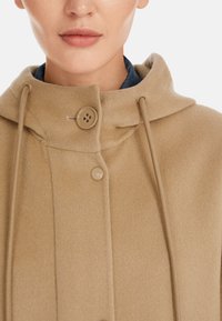 Beige Wollmantel mit Kapuze, ausgestattet mit einem Knopfverschluss und Zugbands-Details. Glatte Textur, minimalistisches Design und beiger Farbton.