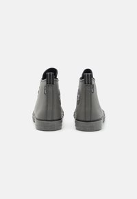 Scarpe alte grigie con una texture liscia, suole in gomma e linguette posteriori per il sollevamento. Presentano un logo a stella Converse ben visibile sul tallone.