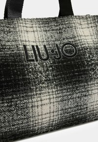 Grå og hvid ternet tote bag med en blød tekstur, der har et sort præget "LIU·JO" logo og robuste sorte stofhåndtag.