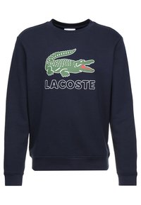Mörkblå bomulls sweatshirt med en stor grön krokodil-logotyp och "LACOSTE" text i vitt. Rund hals, långa ärmar och ribbade cuffs.