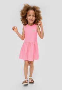 Rosa ärmelloses Kleid mit einem gerafften Rock, das ein kleines grünes Erdbeerdesign auf der Brust hat. Getragen mit leichten Sandalen.
