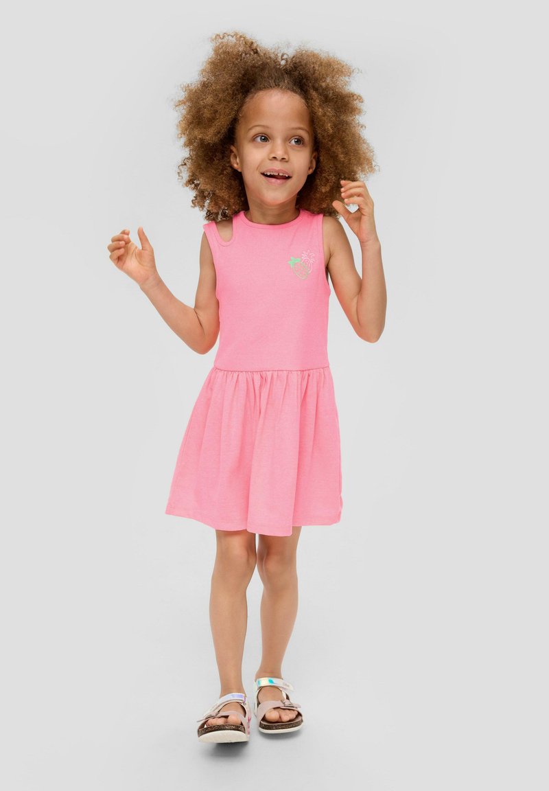 Rosa ärmelloses Kleid mit einem gerafften Rock, das ein kleines grünes Erdbeerdesign auf der Brust hat. Getragen mit leichten Sandalen.