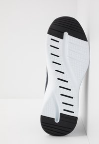 Suola di scarpa atletica in bianco e nero con ammortizzazione bianca testurizzata, motivi di presa in gomma nera e scanalature di ventilazione lungo i lati.