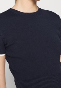 Haut en maille à manches courtes de couleur marine avec une texture côtelée, un col rond et une bordure blanche contrastante sur les manches. Design ajusté.