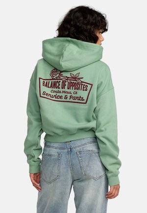 Felpa verde con un grande design stampato sul retro che presenta rose e testo. Maniche a costine e vita a costine, abbinata a jeans in denim chiaro.