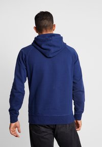 Felpa blu navy realizzata in morbido tessuto, con un cappuccio ampio, polsini e orlo a costine, con una vestibilità comoda e maniche raglan.