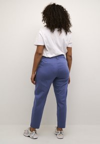 Pantaloni azzurri chiari con una vestibilità slim, dotati di tasche posteriori e una texture liscia, abbinati a una maglietta bianca semplice e sneakers grigie.