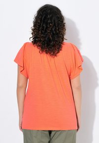 Košile s krátkým rukávem, pohled zezadu na živě oranžové tričko s volány na ramenou, vyrobené z lehké látky.