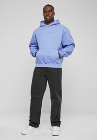 Svijetloplava hoodie s prednjim džepom i kapuljačom s uže, u kombinaciji s tamno sivim hlačama i bijelim tenisicama. Jednostavan, ležeran dizajn.
