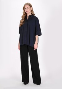 Marineblaue übergroße Bluse mit durchgehender Knopfleiste und Kragen, kombiniert mit weit geschnittenen schwarzen Hosen. Glattes Material und lockere Passform.