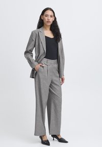 Grå skræddersyet jakkesæt bestående af en struktureret blazer og brede bukser med en subtil tekstur. Båret over en sort top med stilfulde sorte hæle.