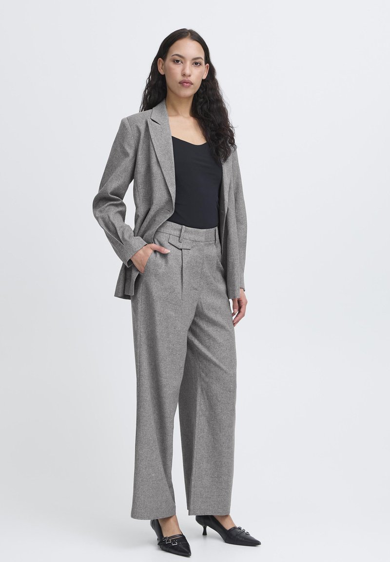 Grå skræddersyet jakkesæt bestående af en struktureret blazer og brede bukser med en subtil tekstur. Båret over en sort top med stilfulde sorte hæle.