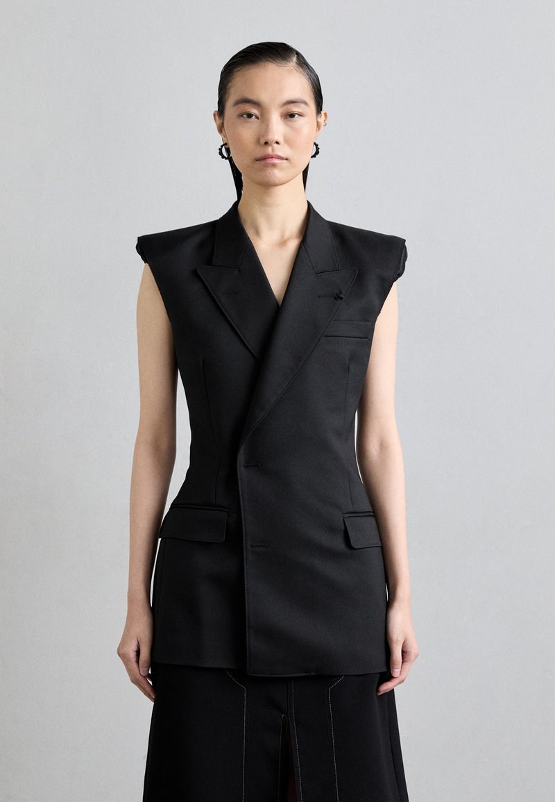 Čierny strihový vest s výraznými ramennými vyvýšeniami, dvojitými prednými vreckami a výstrihom do V, vyrobený z hladkej látky so subtilnými švovými detailami.
