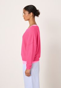 Pull rose duveteux à épaules tombantes et ourlet côtelé, superposé sur un haut rose. Associé à un pantalon bleu clair à rayures.