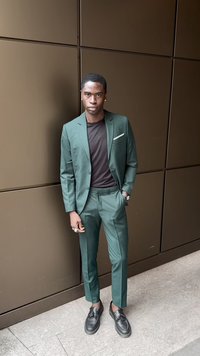 Green suit with a fitted design and tailored trousers. Paired with a black shirt and black loafers. Simple pocket square detail.