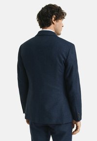 Navy Blazer aus strukturiertem Stoff, taillierter Passform und mit Reverskragen. Es gibt drei Knöpfe an jedem Manschette und einen Schlitz im Rücken.