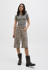 Pelēks ribots īss piedurkņu tops kopā ar leoparda raksta džinsa šortiem. Modele valkā melnus ceļgalu augstus zābakus. Vienkārša fona.