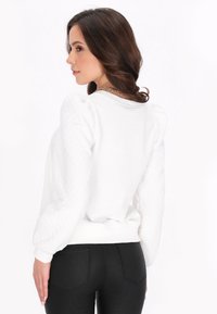 Hvid sweatshirt med puffede quiltede ærmer, ribbet kant og manchetter, rund halsudskæring og en glat bagsidetekstur. Parret med sorte tætsiddende bukser.