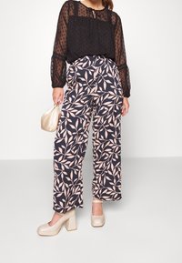 Black sheer blouse with polka dots, paired with wide-leg trousers featuring a navy background and soft pink leaf pattern. Cream block-heeled shoes.