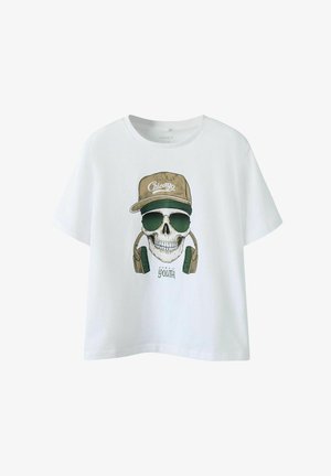 T-shirt en coton blanc avec un graphique de crâne portant des lunettes de soleil et des écouteurs, complété par une casquette beige portant l'inscription "Chicago".