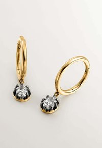 Los pendientes de aro dorados presentan una gran piedra facetada y clara suspendida de una base negra con forma floral, ofreciendo contraste y textura.