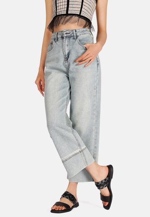 Jeans a vita alta e gamba larga di colore azzurro chiaro con cuciture visibili. Indossati con sandali neri con cinturini a fantasia.